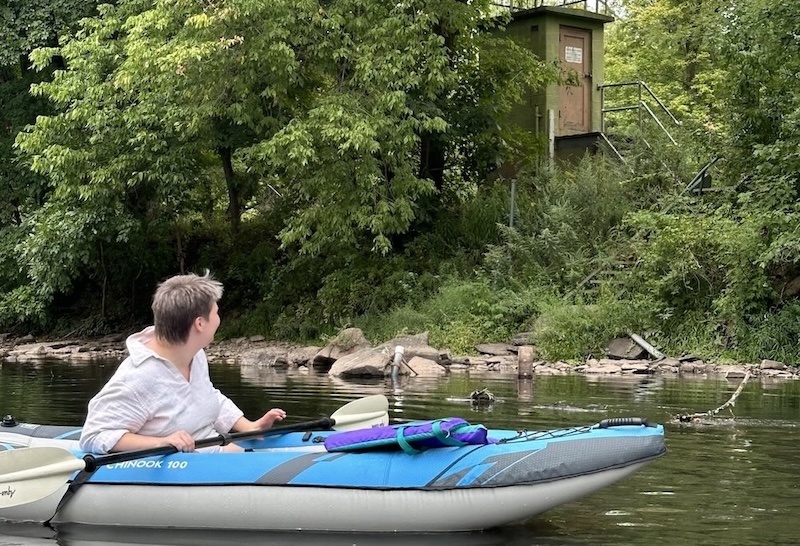 Paddler in kayak looking at nearby streamgage on bank of the Perkiomen Creek.